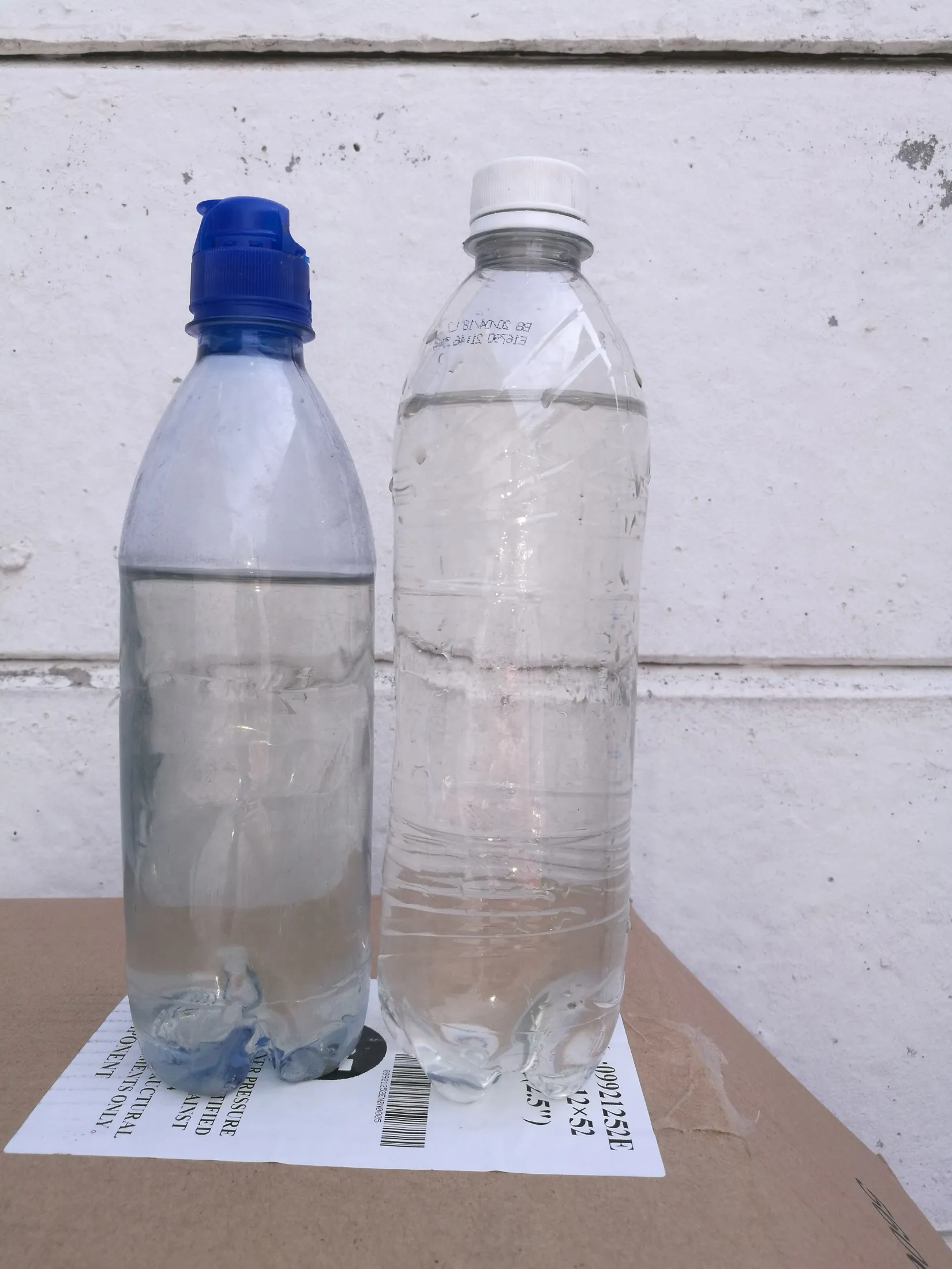 Two water bottles standing against a white wall for comparison