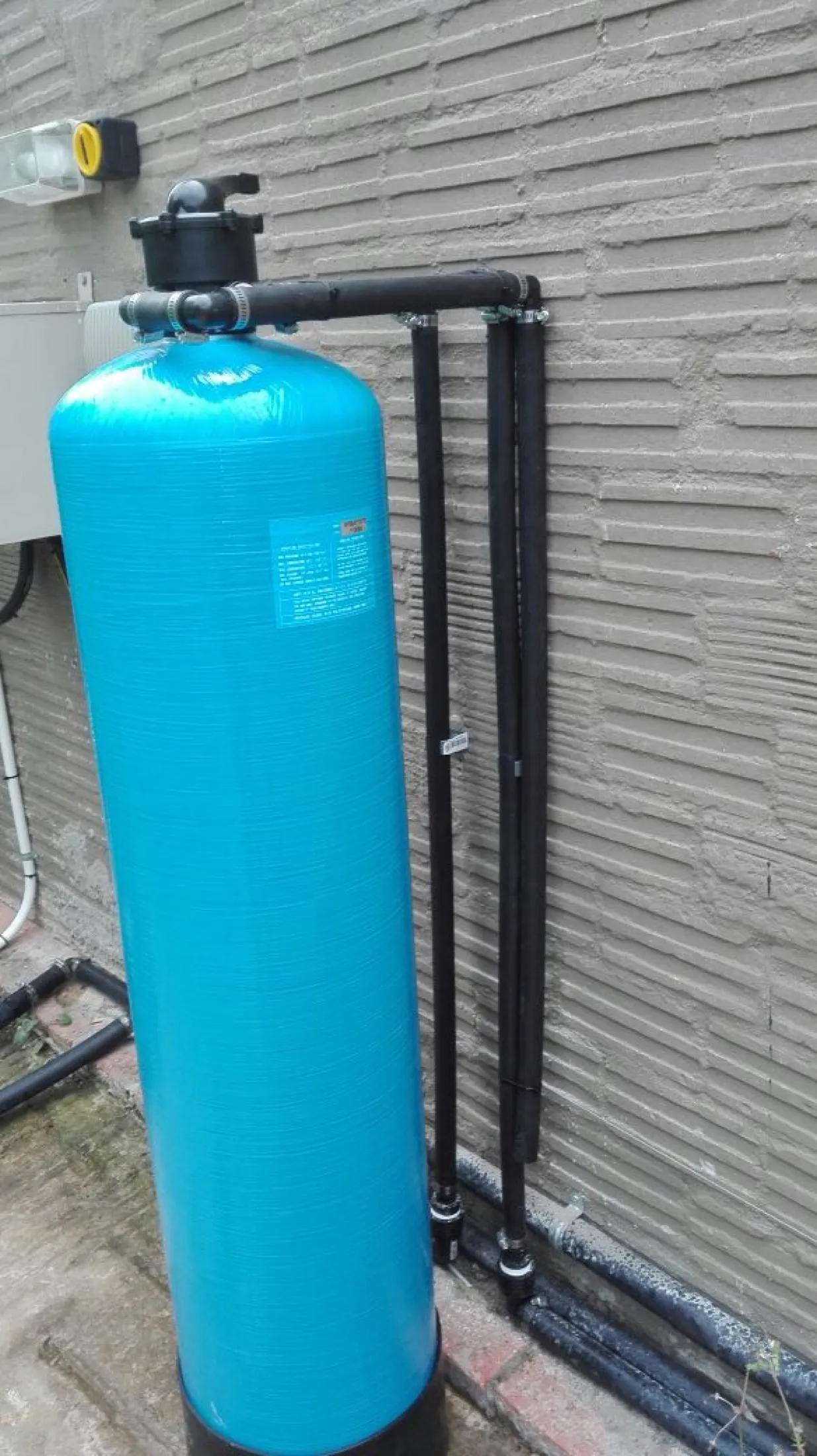Tall blue filter vessel with multi-port valve against a wall
