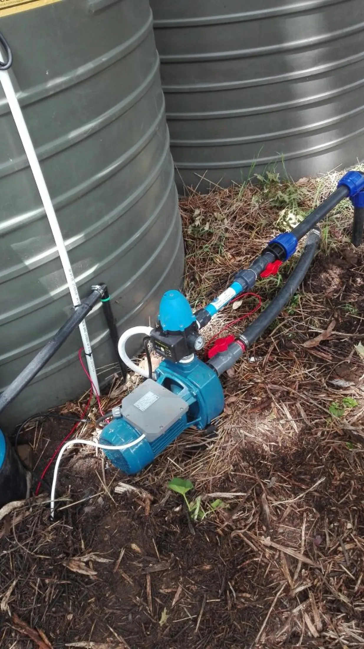 Booster pump connected to tank pipework in a garden