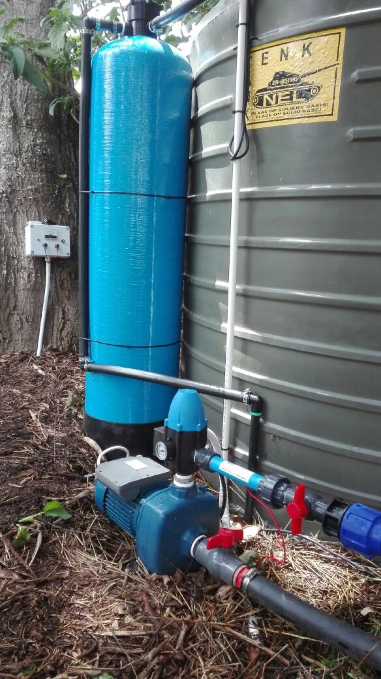 Filter vessel and pump beside a large corrugated water tank