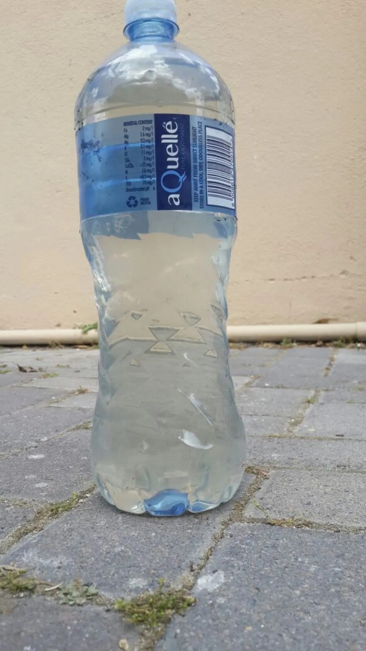 A bottle of clear water standing on a paved surface